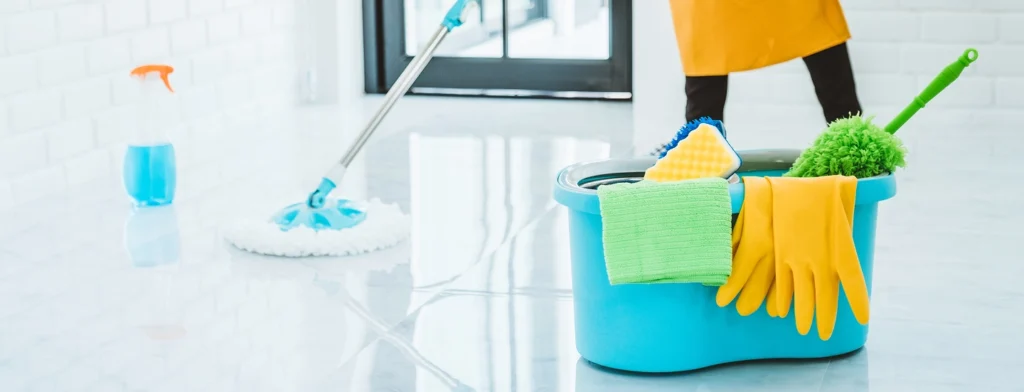 Limpeza profissional a esfregar um chão brilhante com produtos e equipamentos de limpeza nas proximidades.
